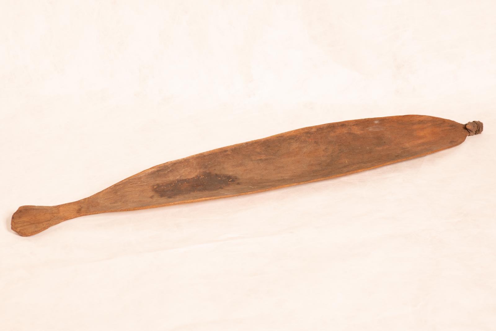 Carved wood spear thrower, Mirra, with small round handle grip tapered to paddle shaped body and rounded end. Small pointed piece is attached to end with tendon bindings wrapped around.