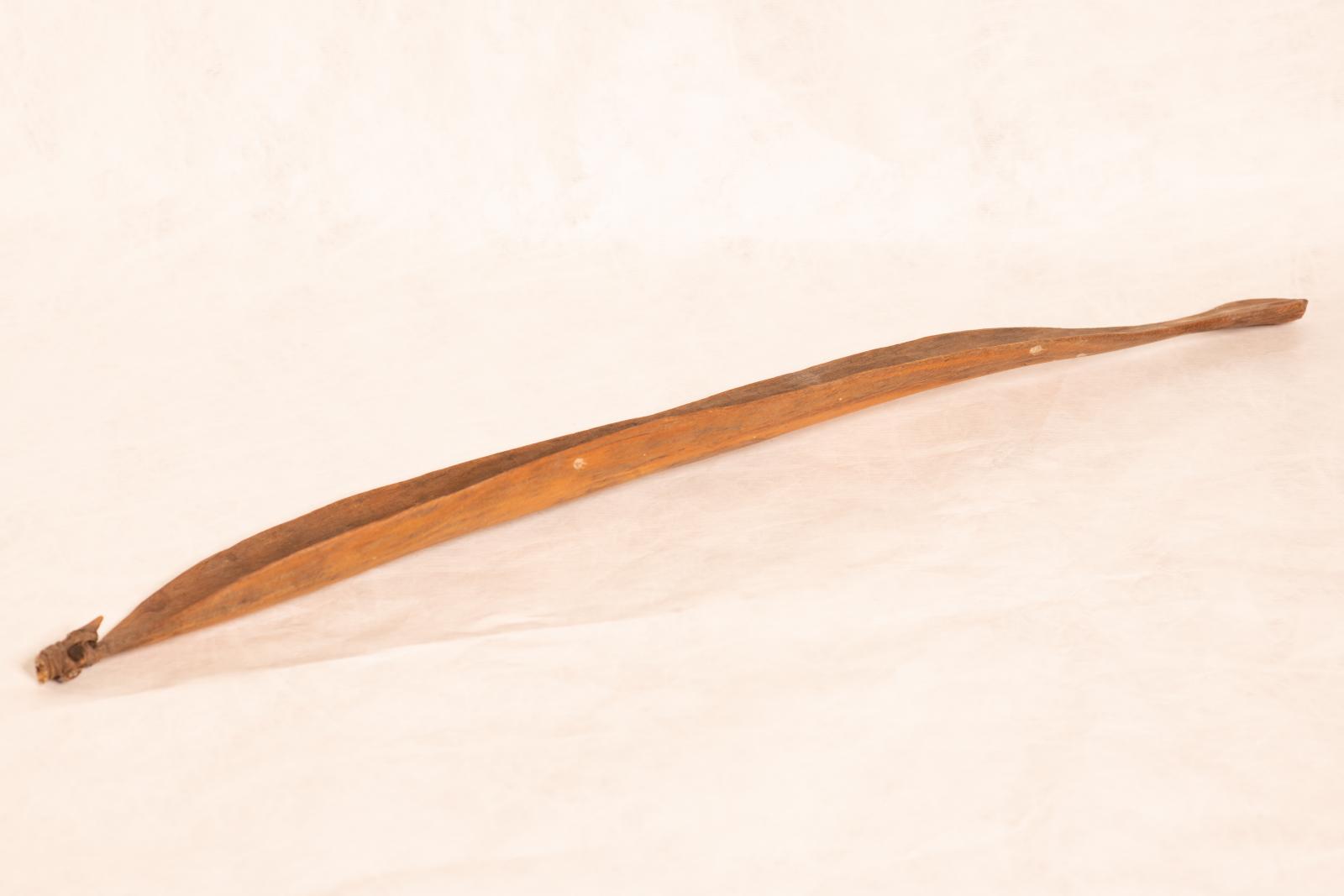 Carved wood spear thrower, Mirra, with small round handle grip tapered to paddle shaped body and rounded end. Small pointed piece is attached to end with tendon bindings wrapped around.