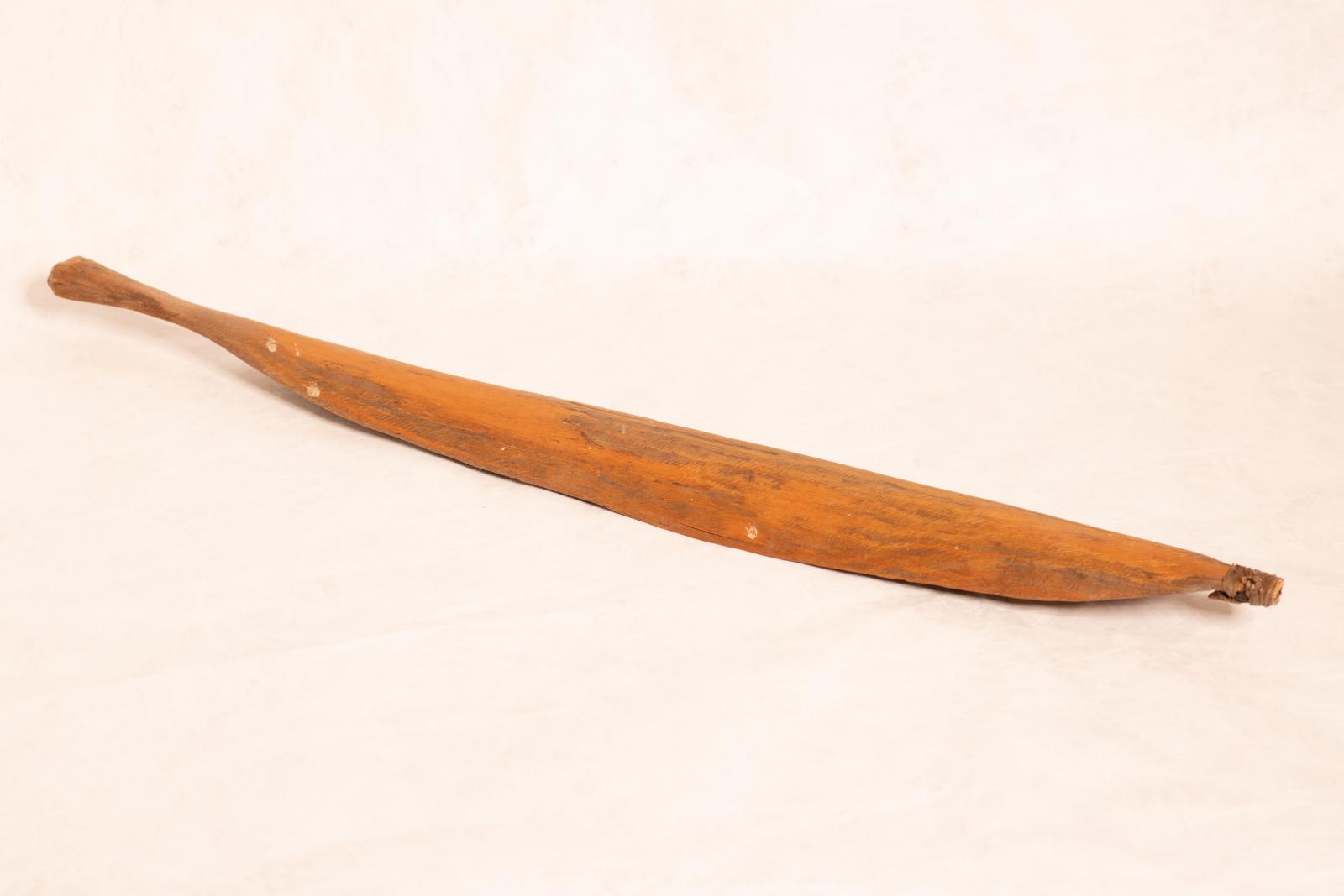 Carved wood spear thrower, Mirra, with small round handle grip tapered to paddle shaped body and rounded end. Small pointed piece is attached to end with tendon bindings wrapped around.