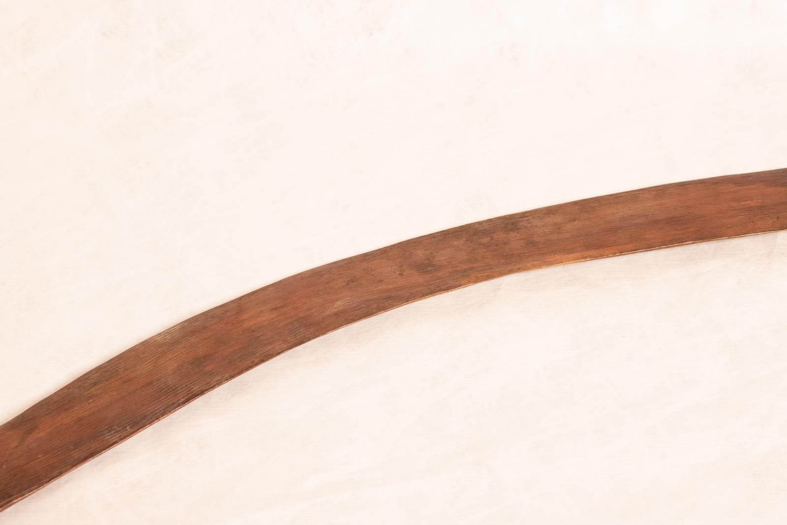 Carved wooden boomerang with rounded edges and ends. Raised linear pattern running from end to end along length of boomerang.