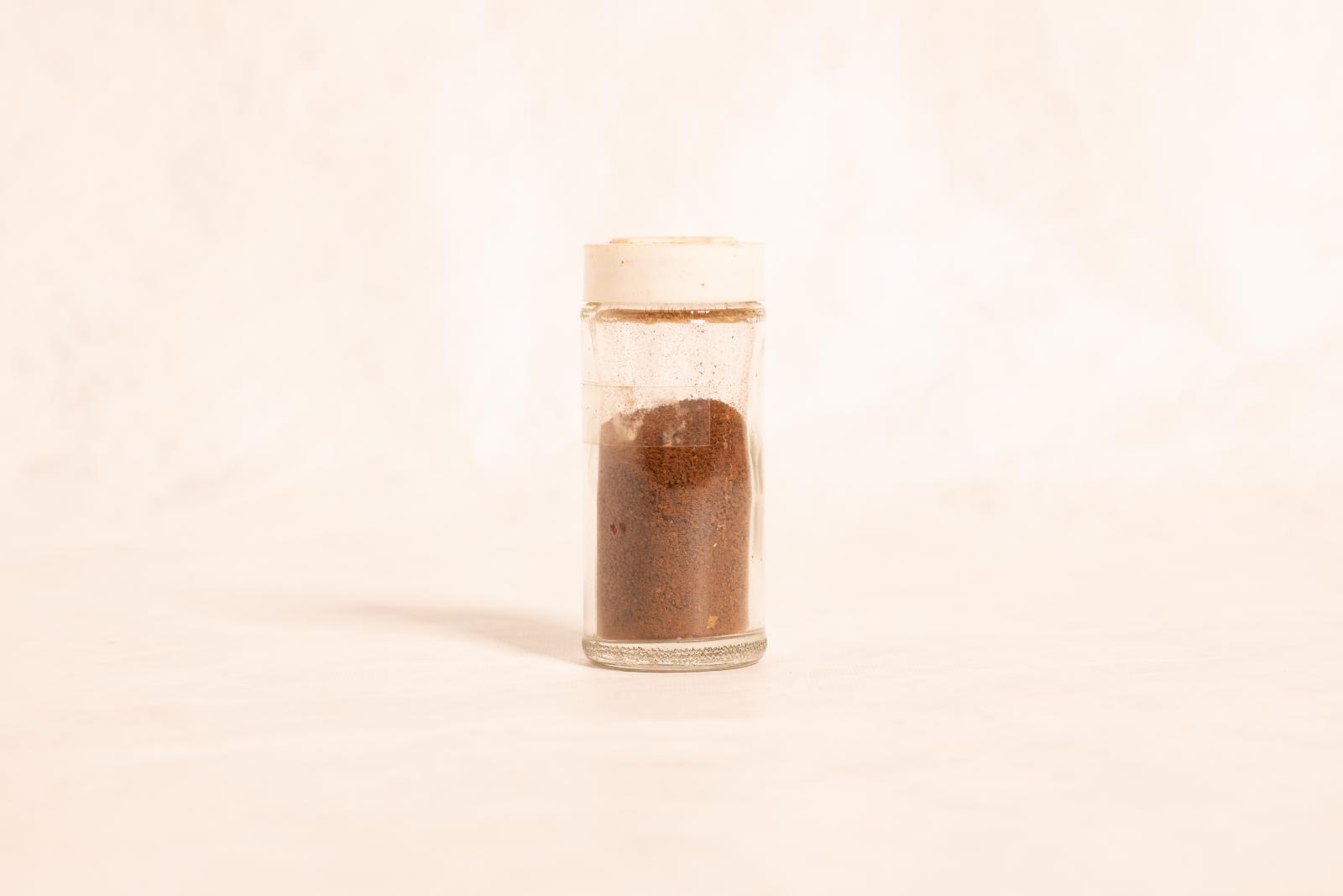 Clear glass jar with white plastic lid and dried wattle seeds inside.