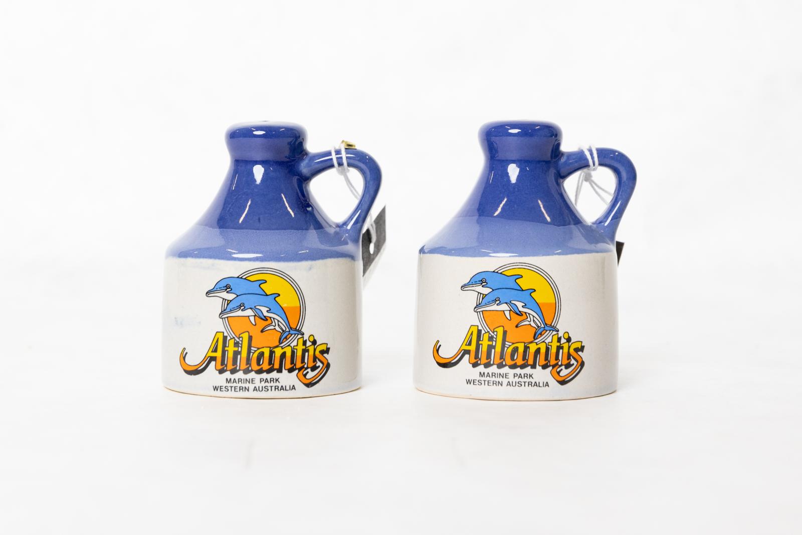 Two white and blue jugs with an Atlantis Marine Park logo, consisting of two dolphins jumping through the air in front of a yellow and orange circle.