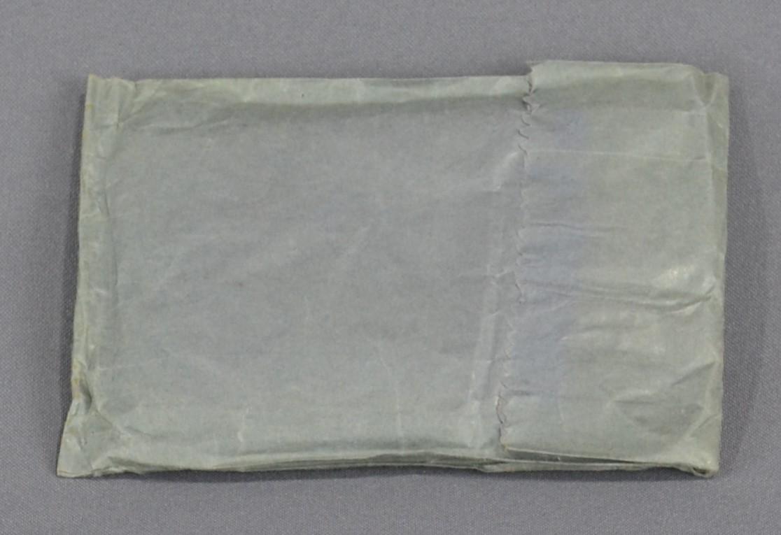 Reverse side of triangular bandage package which is grey paper envelope with opening folded over and adhered in place on the right