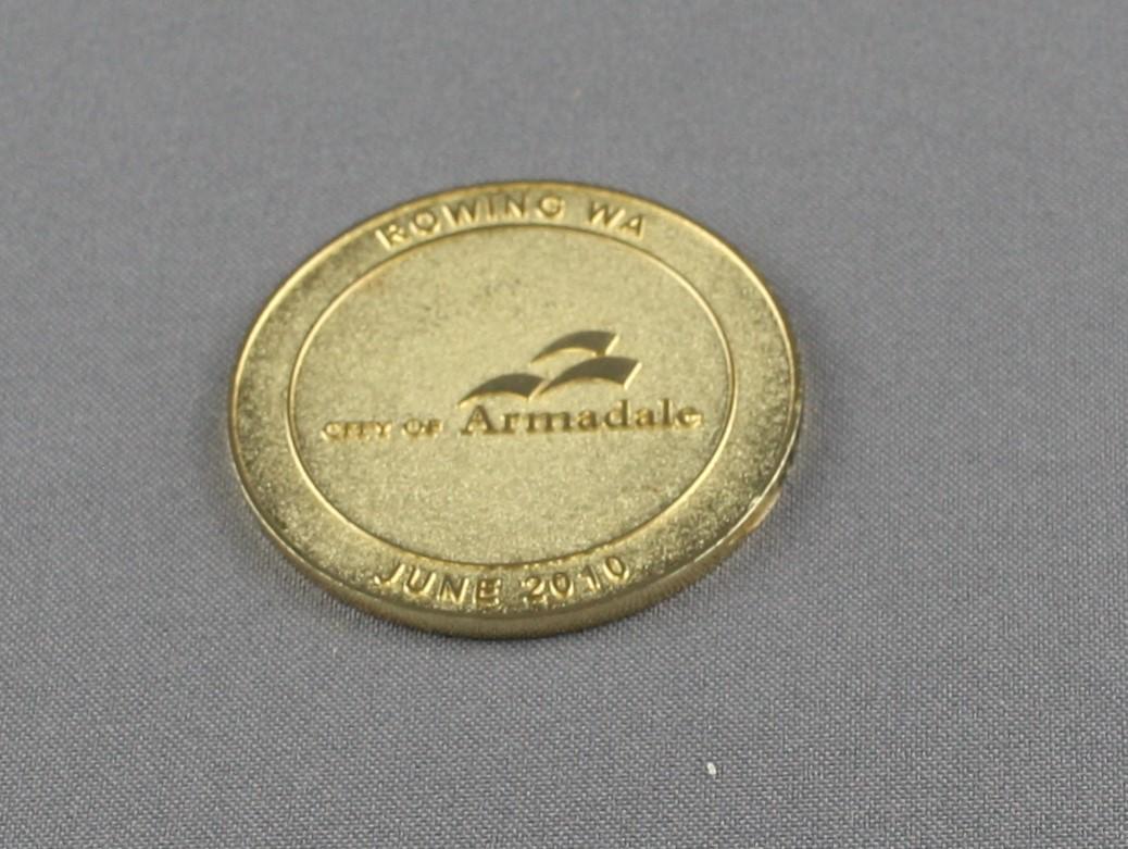 Front of the round commemorative medal which is made of a gold coloured metal with the City of Armadale name and logo in the centre and the text "Rowing WA" at the top and "June 2010" at the bottom of the medal