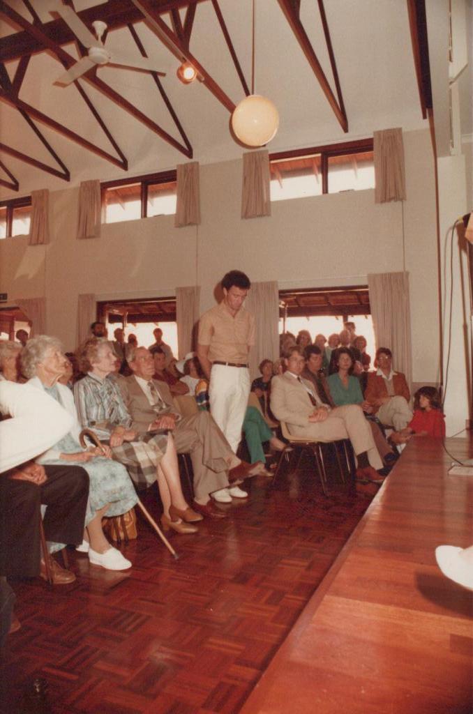 people in a large hall with the front of a stage just visible