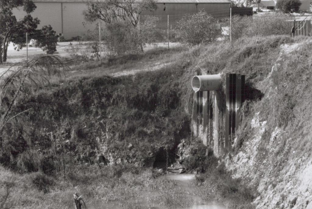 black and white photo of water coming out of a pipe into a waste pond