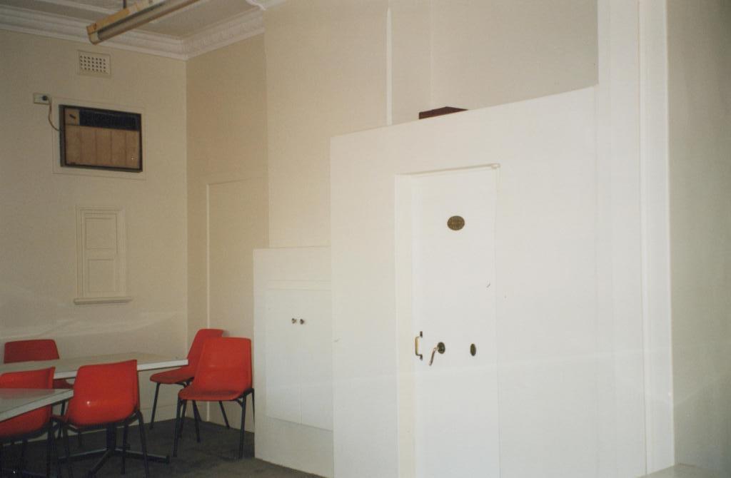 photograph of room. Room contains red chairs and a white table.