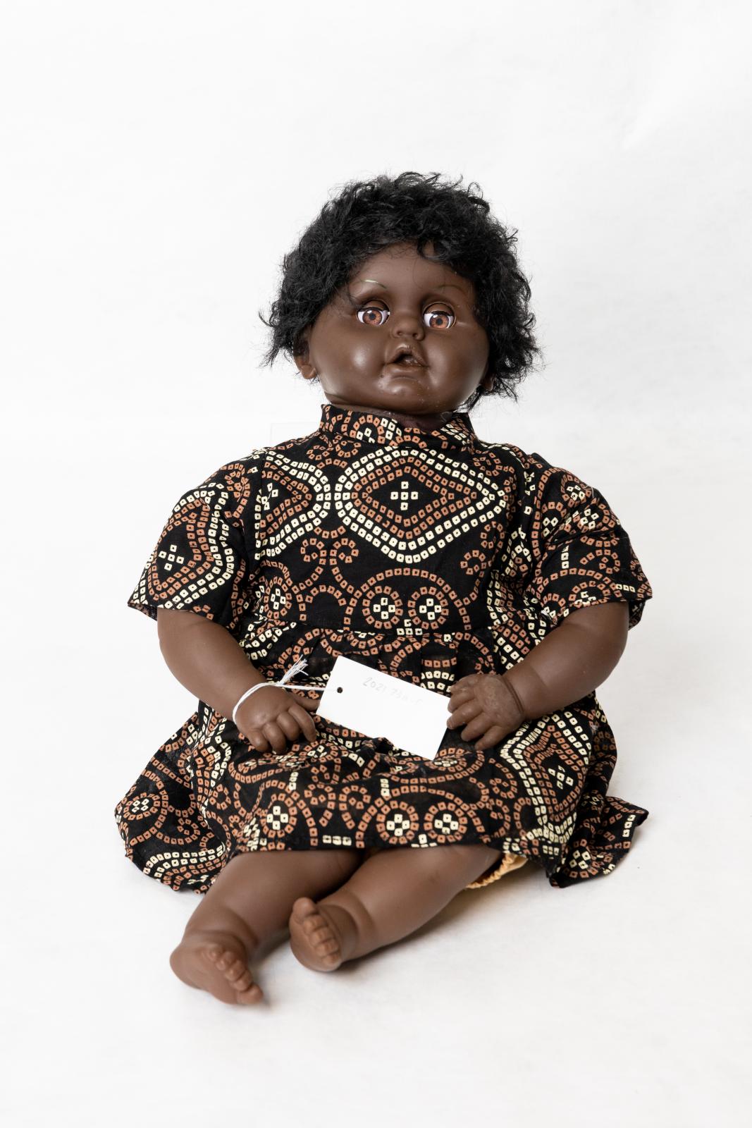 Aboriginal infant girl doll. Black tunic with print and plain pastel yellow shorts.