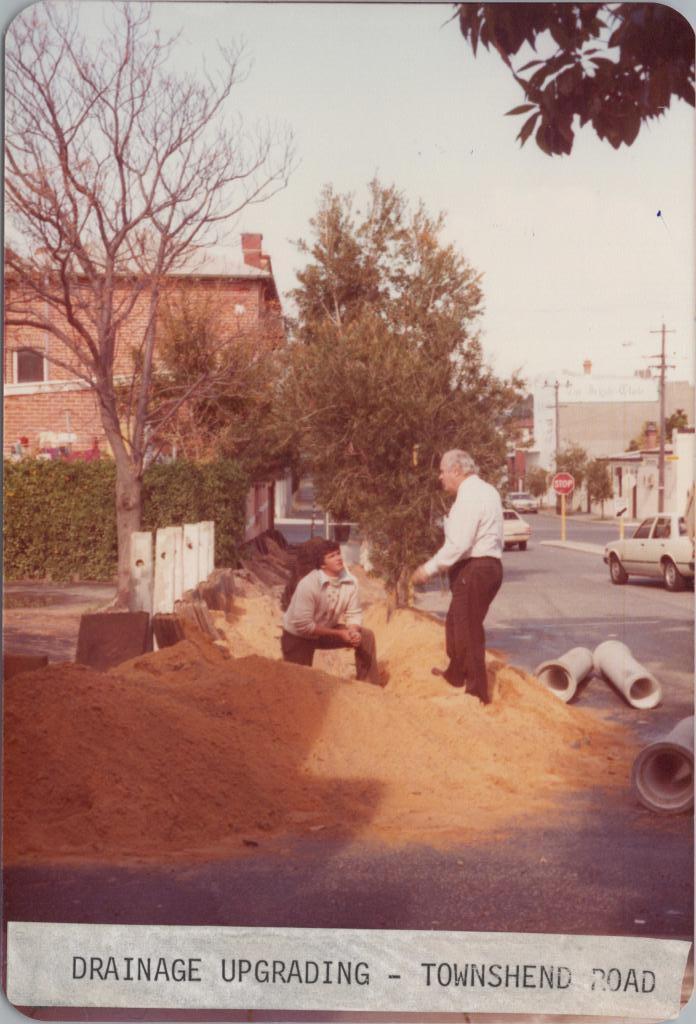 photograph of two men talking on a pile of yellow sand