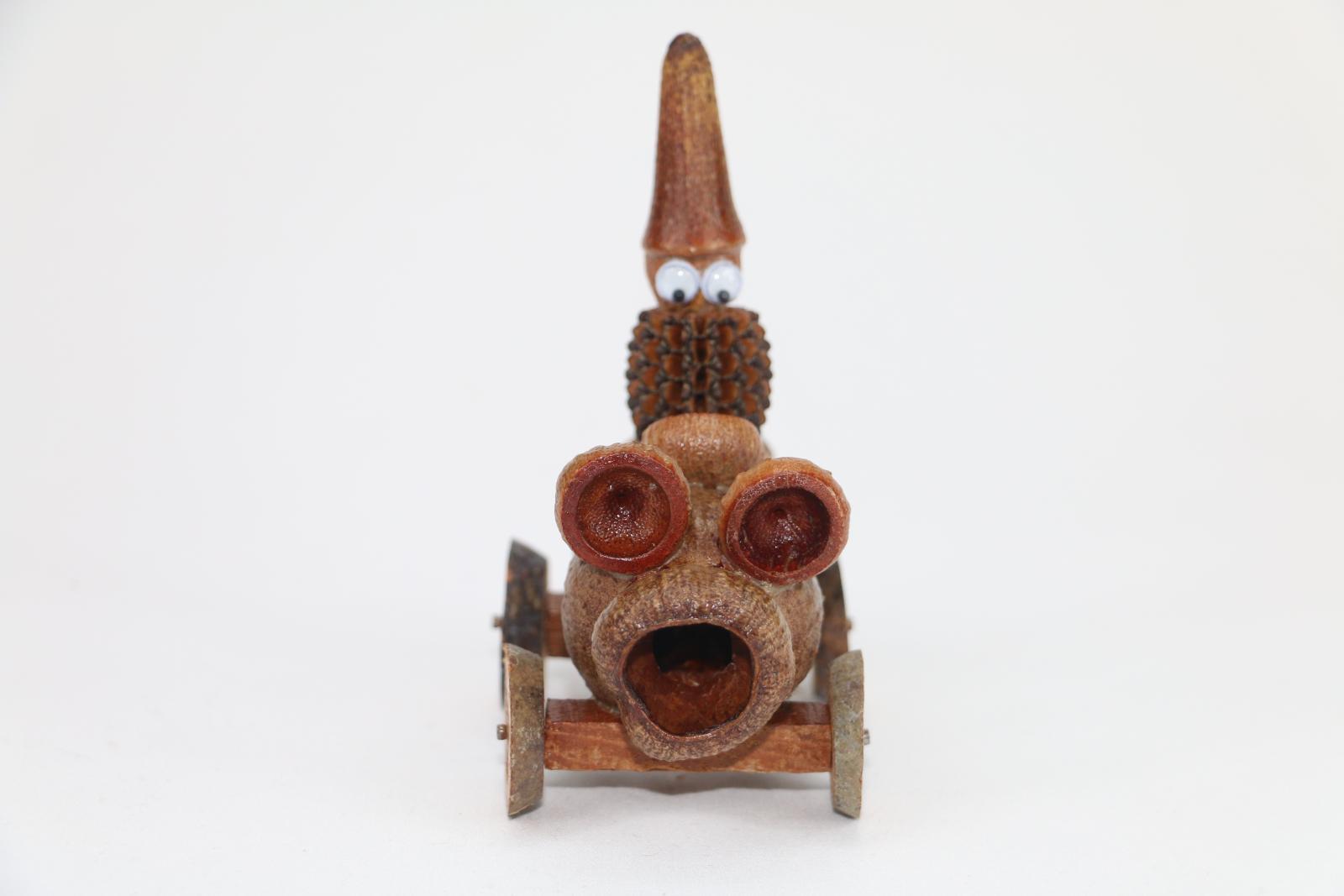 The front view of a Gumnut man with googly eyes, in a car. All made from different plant material.