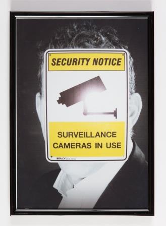 Black and white photo of a front facing male figure, with bright yellow security surveillance sign covering his face