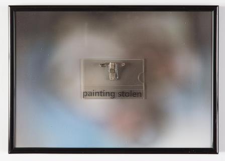 Image of what could be a plastic wall hook with text 'painting stolen' below on a blurry, out of focus background