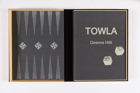 Open book showing front and back cover. The front cover is shown on the right with white text "Towla" in the centre, and the artist's name below. Two white dice are depicted below the text towards the right of the cover. The back cover is depicted on the left and shows a black and grey backgammon board