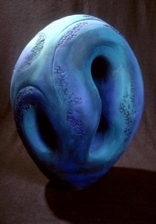 Oval shaped sculpture with two divots on the right and left of the sculpture. Glazed in blue and purple. 