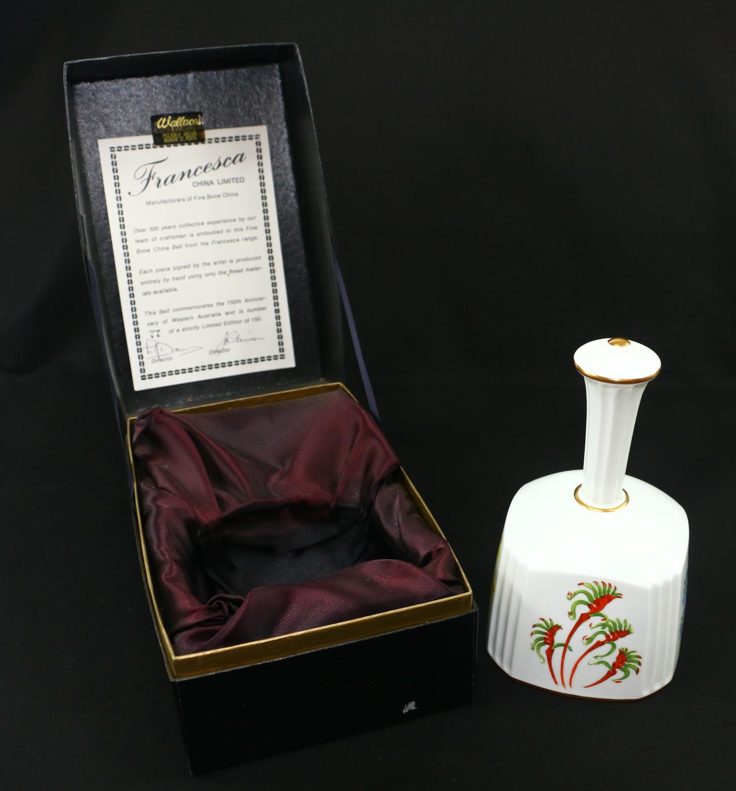 A rectangular black cardboard box with a gold rim around the top. Black satin lined. Inside is a square, white, fine-bone china bell.