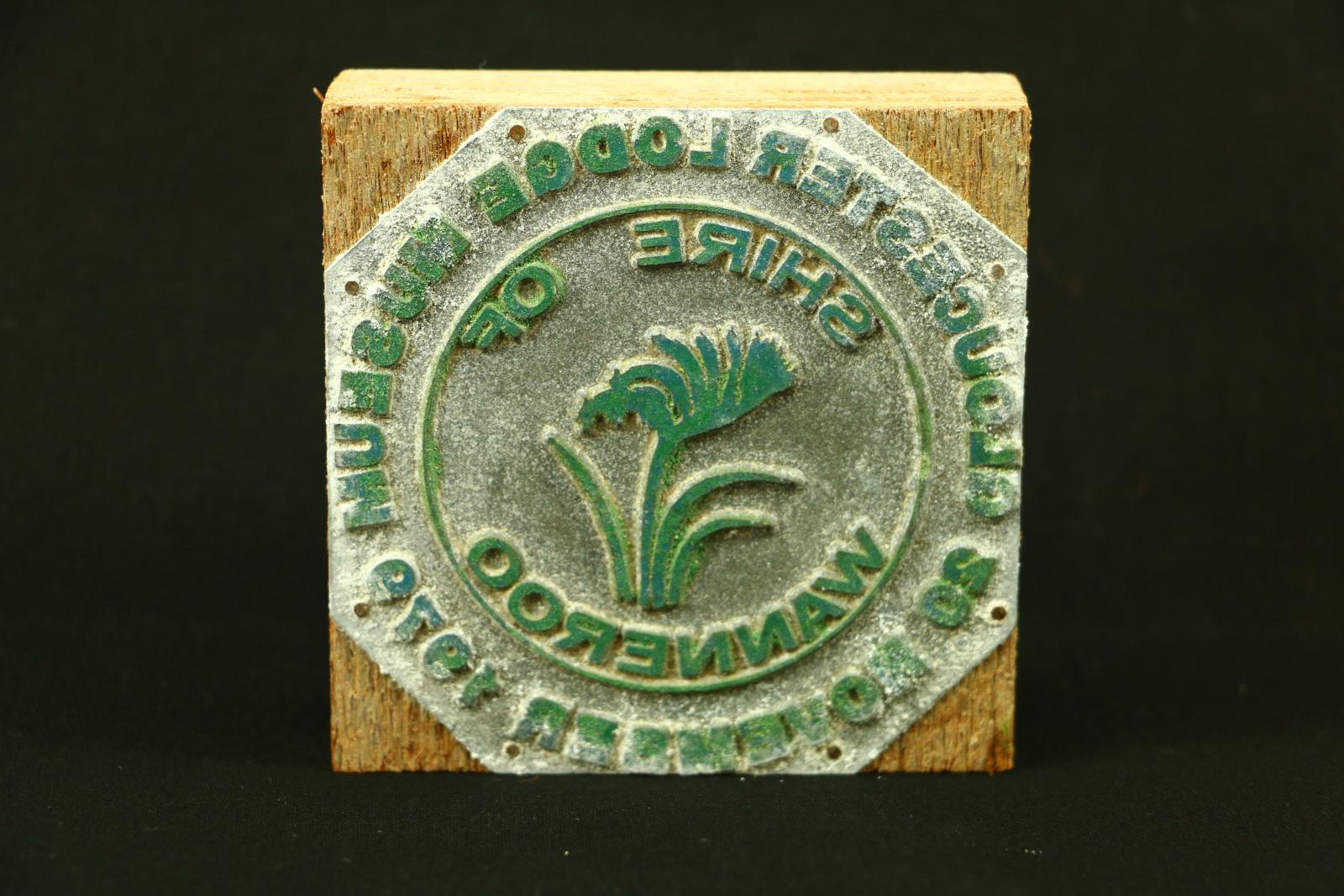 A square wooden block, with a rubber stamp attached to one side. It has a circular pattern and around the edge says "GLOUCESTER LODGE MUSEUM 20 NOVEMBER 1979". "SHIRE OF WANNEROO" is written within an inner circle in a circular design and the City of Wanneros's emblem, the Kangaroo Paw.