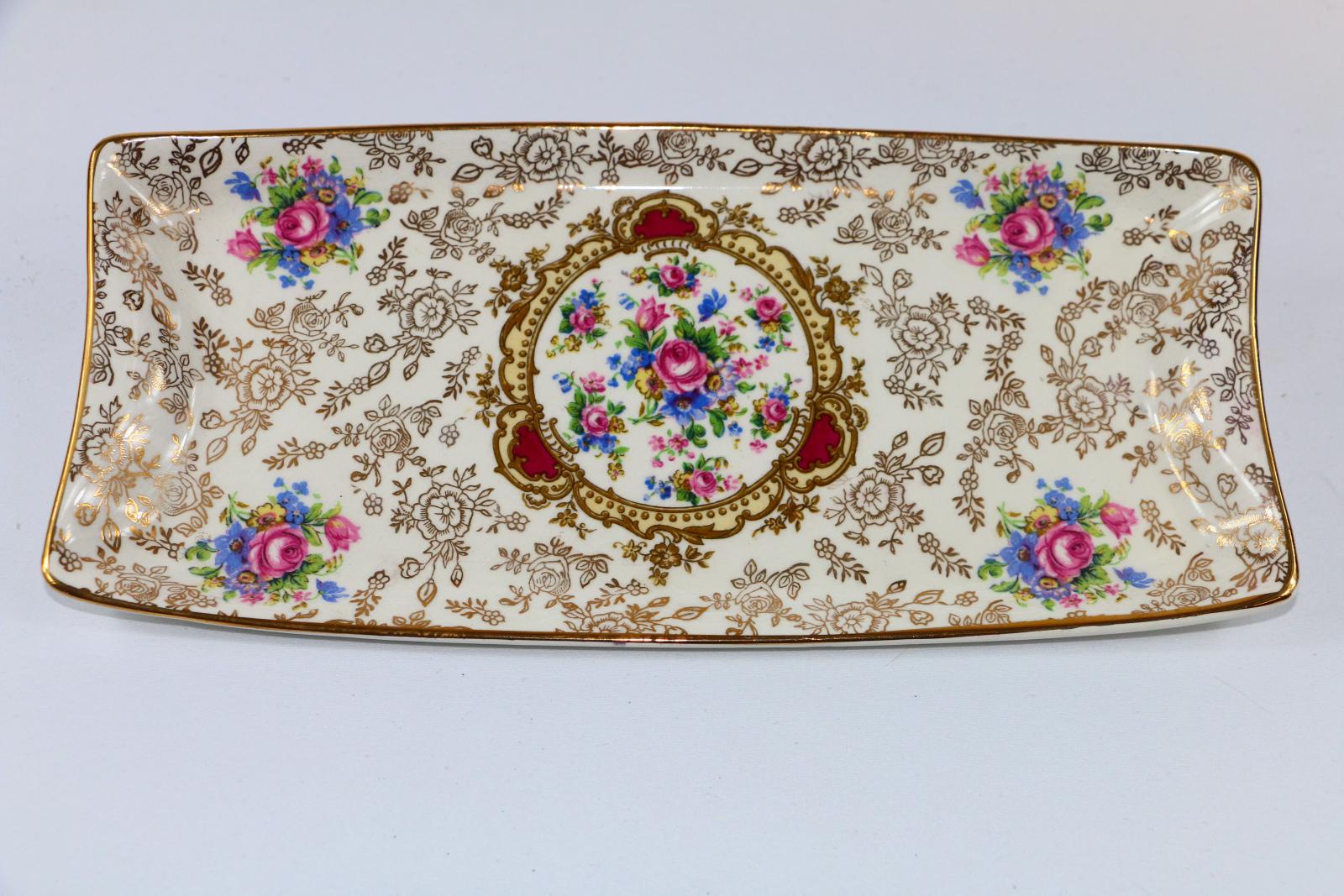 A rectangular white ceramic sandwich platter with four repeated hand painted floral designs, a circular design in the centre filled with a floral design, there is a gold floral design over the rest of the platter.