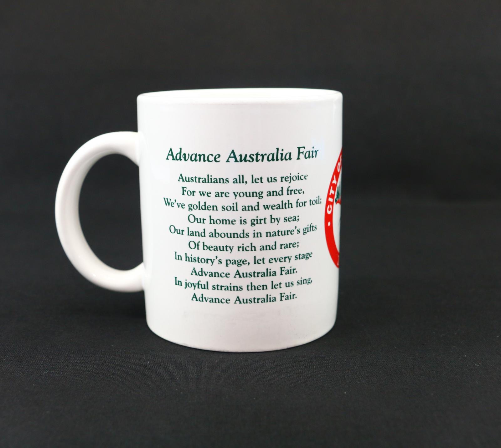 A round, white ceramic, City of Wanneroo, mug. On the left-hand side of the mug is the first verse of Advance Australia Fair written in green.