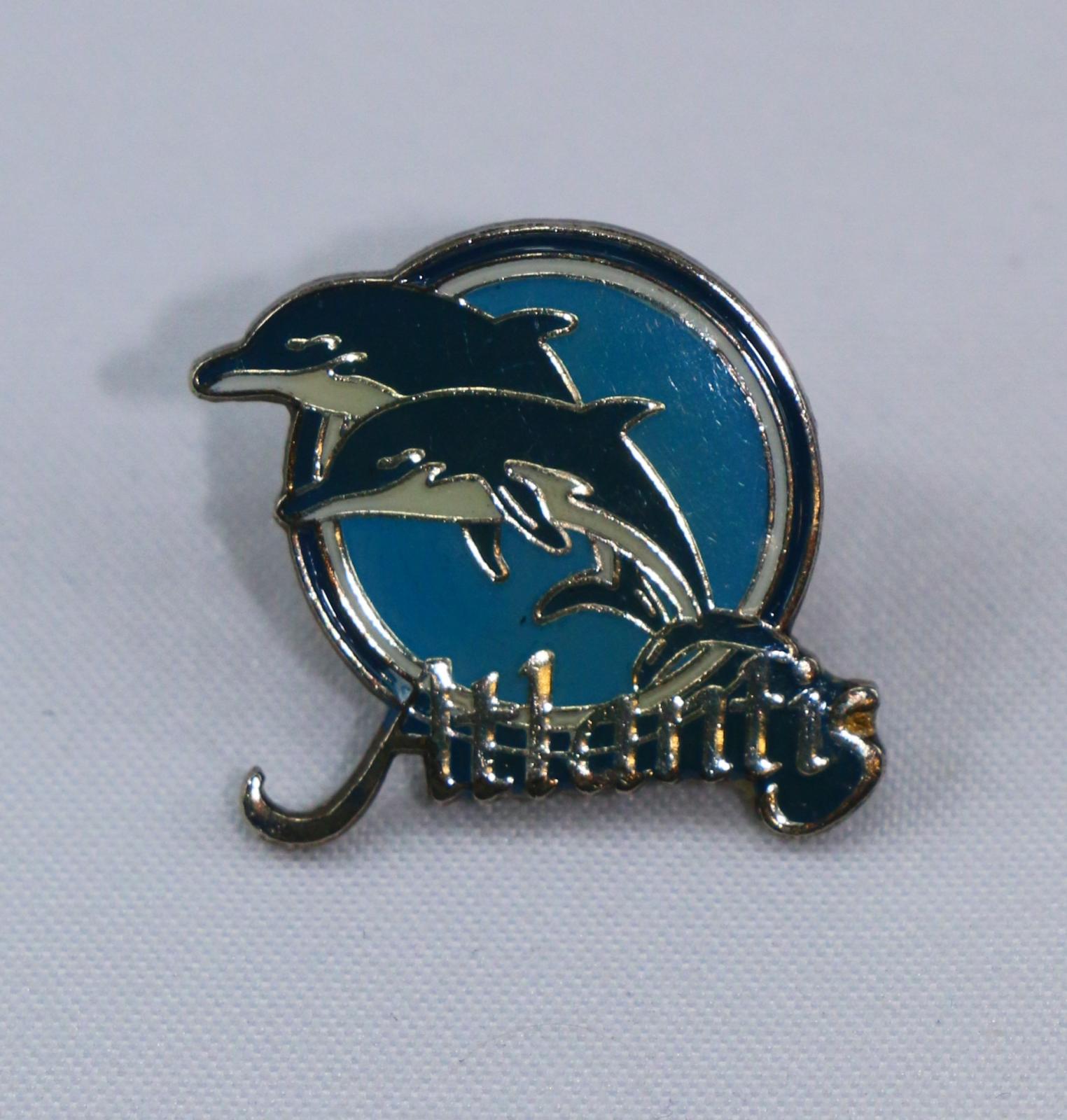 Atlantis lapel pin with two blue and white dolphins and 'Atlantis' written across the bottom.