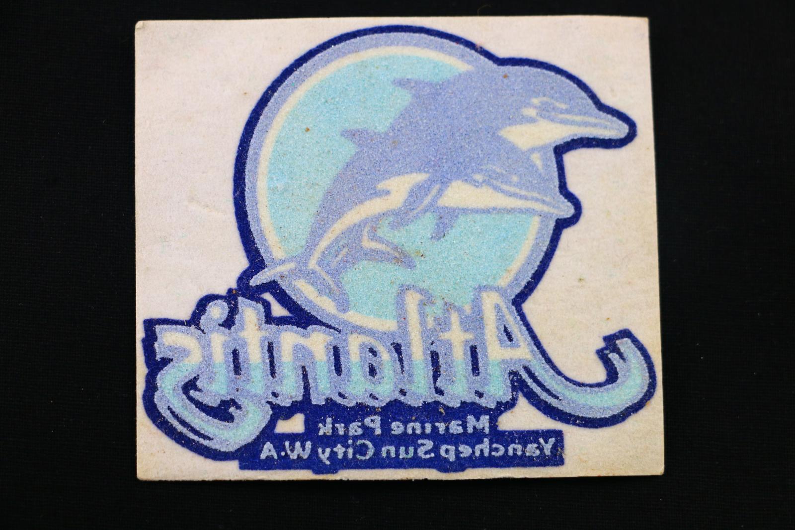 A blue and white square iron-on flocked transfer patch of dolphins with Atlantis brand.