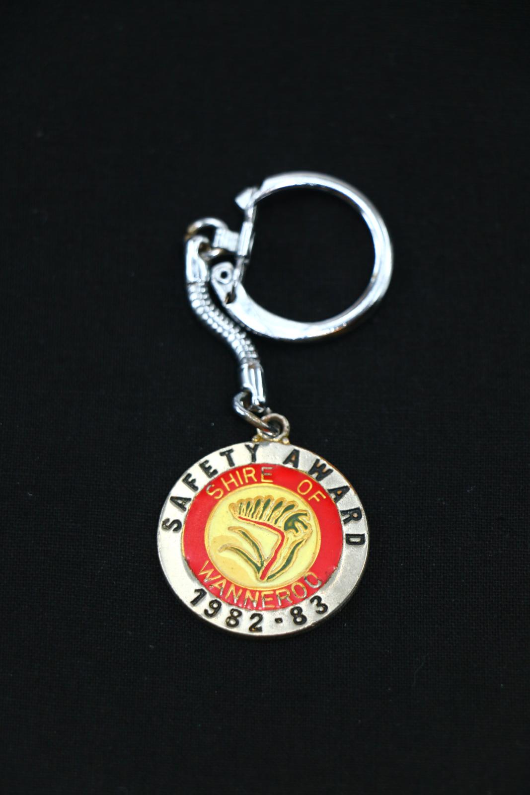 A metal and enamel disc with words 'SAFETY AWARD 1982 - 83' 'SHIRE OF WANNEROO' encircling the kangaroo paw emblem. A solid chain and circular clasp are attached at top of disc.