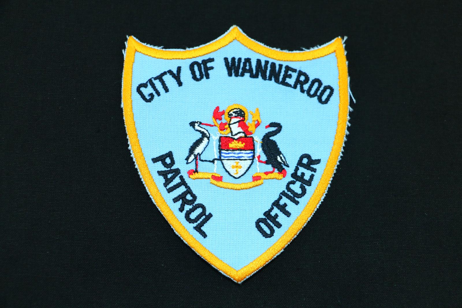 A three point shield shaped cloth patch. It has a blue background with letters stitched in black thread that read 'CITY OF WANNEROO' 'PATROL OFFICER'. The crest is in red, black and yellow thread and there is a yellow border around the patch.