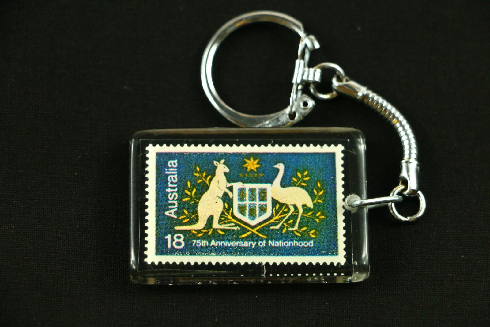 A rectangular plastic and metal keyring for the 75th Anniversary of Australian Nationhood. Inside the plastic of the keyring is a rectangular postage stamp which has a blue background, a white boarder around the edge and a kangaroo and emu holding a shield in the centre. Up the left side of the paper in white letters is 'Australia'. Along the bottom edge also in white letters is '18 75th Anniversary of Nationhood'.