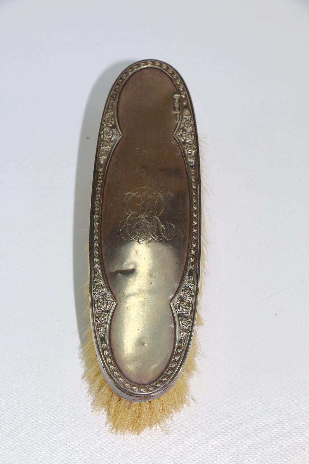 The back of a silver clothes brush with decorative edge and K.R engraved in the centre