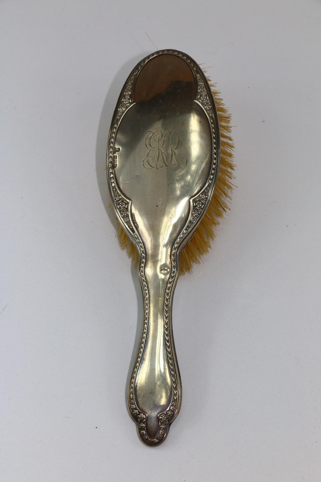 The back of a silver hairbrush with decorative edge and K.R engraved in the centre.