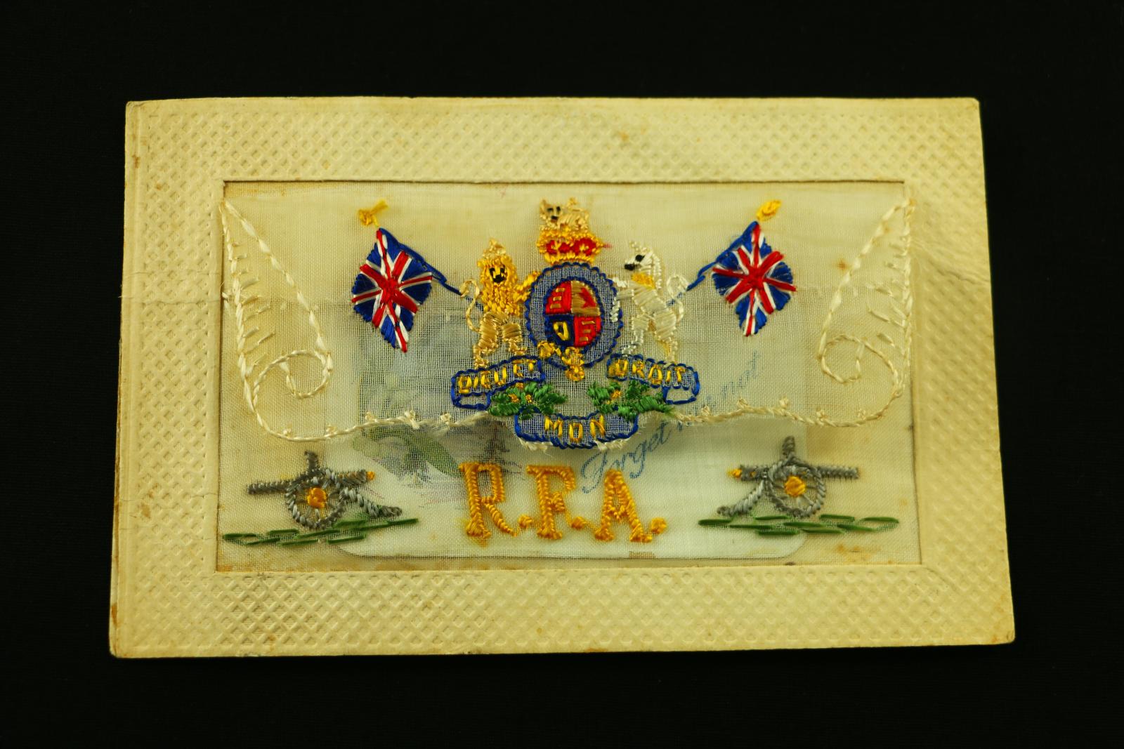 A rectangular, cardboard and embroidered, postcard R.F.A. UK crest and two small cannons on bottom corners. Inside the embroidered envelop is a small rectangular white card displaying a small branch of blossom with the words 'Forget me not' written in blue ink.