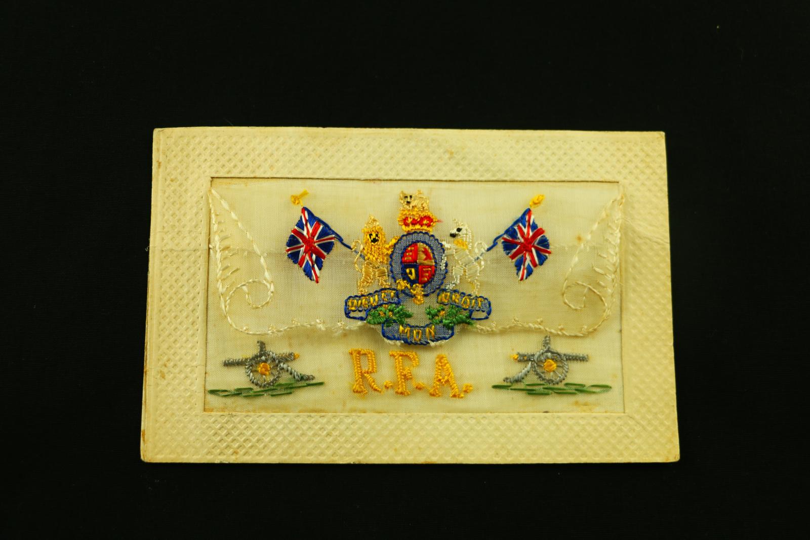 A rectangular, cardboard and embroidered, postcard R.F.A. UK crest and two small cannons on bottom corners.