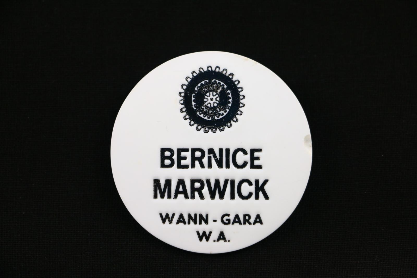 Circular, white plastic 'Inner Wheel' name badge with black debossed text under Inner Wheel logo. Logo design is two concentric cog wheels with tiny, worn, 'INNER WHEEL' text. Main badge text reads: 'BERNICE MARWICK WANN-GARA W.A.'.