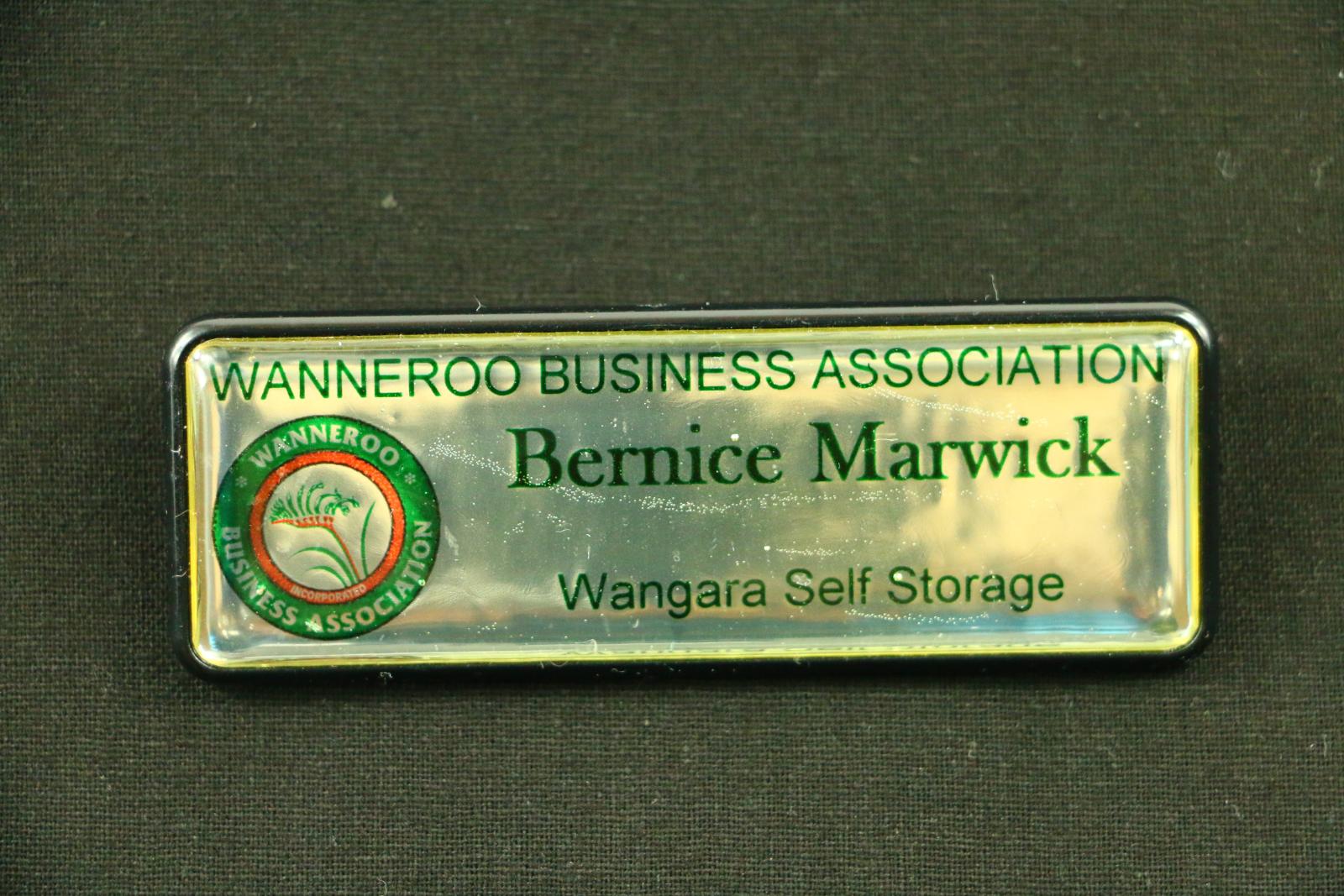 Rectangular, silver coloured plastic name badge with rounded corners. The front of the badge has a black plastic border. The badge reads 'WANNEROO BUSINESS ASSOCIATION', 'Bernice Marwick', 'Wangara Self Storage' in smaller text. On the left hand side is a circular logo that reads 'WANNEROO BUSINESS ASSOCIATION'. Inside the logo is a thinner red border which reads 'INCORPORATED' in a tiny font. At the centre of the logo is a red and green stylised kangaroo paw.