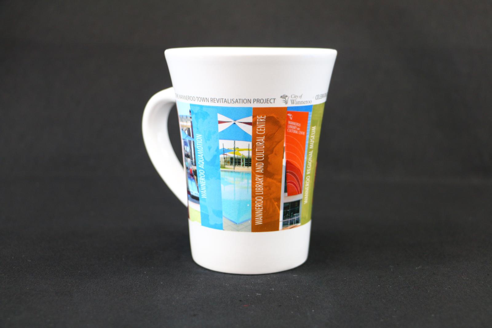 White, ceramic, City of Wanneroo mug with multiple photographic outlines of council locations printed onto the surface around the mug. The top reads 'CELEBRATING THE WANNEROO TOWN REVITALISATION PROJECT'. The first image depicts 'CITY OF WANNEROO AQUAMOTION' and the second image depicts 'WANNEROO LIBRARY AND CULTURAL CENTRE'.