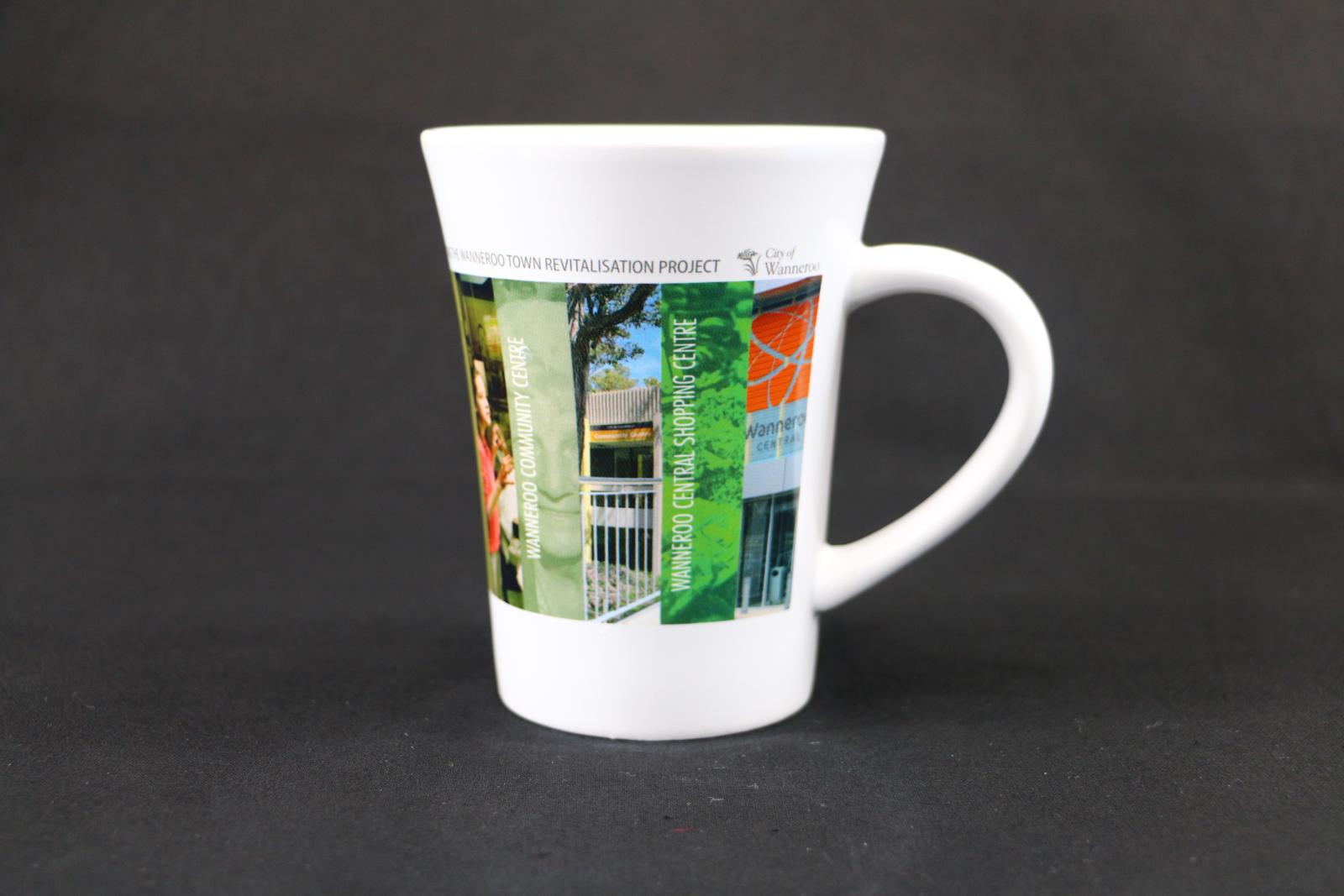 White, ceramic, City of Wanneroo mug with multiple photographic outlines of council locations printed onto the surface around the mug. The top reads 'CELEBRATING THE WANNEROO TOWN REVITALISATION PROJECT'. The first image depicts 'WANNEROO COMMUNITY CENTRE' and the second image depicts 'WANNEROO CENTRAL SHOPPING CENTRE'.