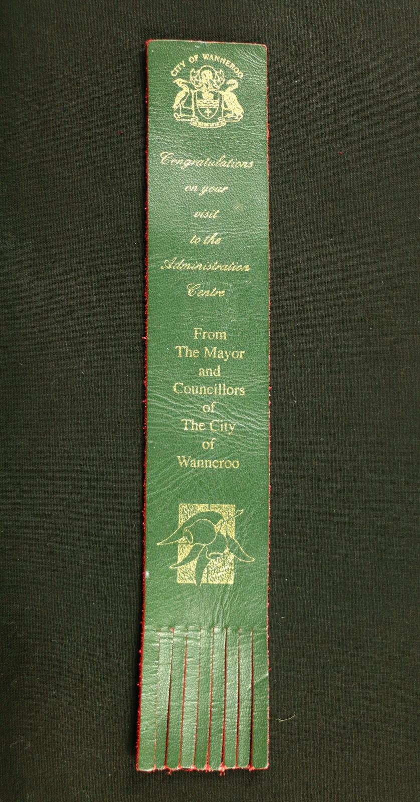 City of Wanneroo bookmark, a thin piece of rectangular leather coloured red on the underside and green on the smoothed top side. Imprinted on the green surface in gold is a small emblem of two water birds holding a shield between them with 'CITY OF WANNEROO' over the top.