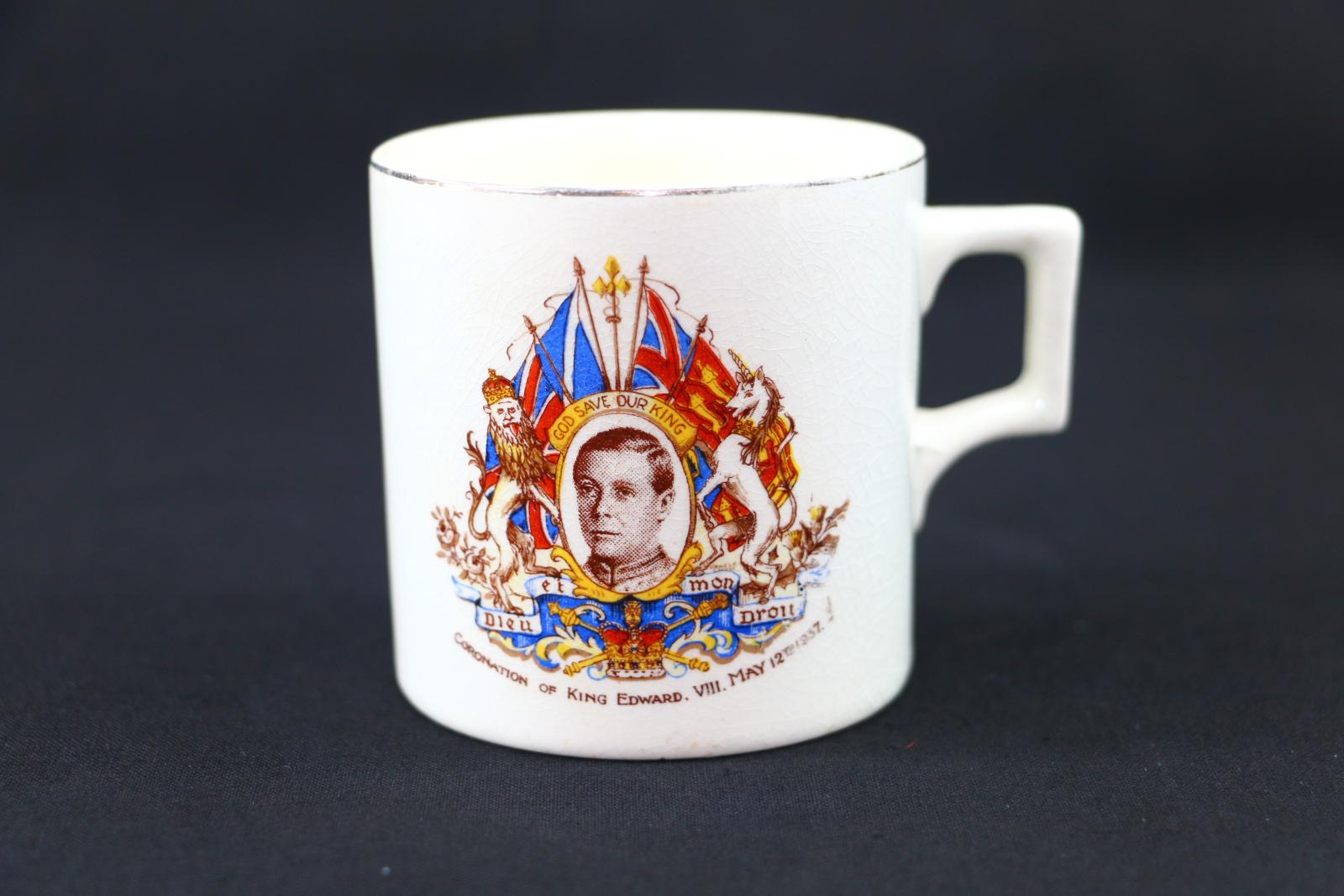 A beige, ceramic, commemorative mug. The cup's rim is lined with gold. The words 'CORONATION OF KING EDWARD, VIII MAY 12TH 1937'. A photo of Prince Edward in the centre and on the left is a stem of two roses, a lion wearing a crown, and an English flag with a Scottish flag above. On the right side of the image is a thistle in bloom, a unicorn, a royal standard flag, and a Union Jack flag above. In a ribbon scroll under the image the words 'DIEU ET MON DROIT. 