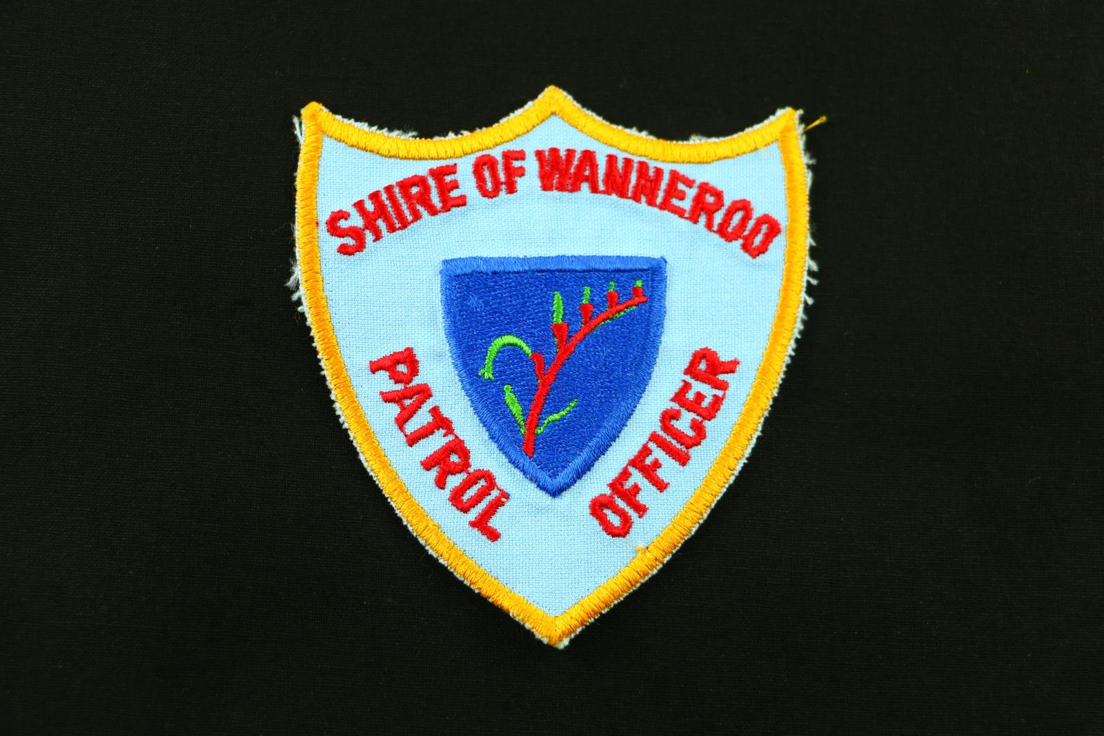 A Shire of Wanneroo Patrol Officer cloth patch. It is a three-point shield shape with a blue background and yellow stitched edging. The words 'SHIRE OF WANNEROO' and 'PATROL OFFICER' are in red thread. In the centre is a dark blue shield which contains a red and green kangaroo paw. 