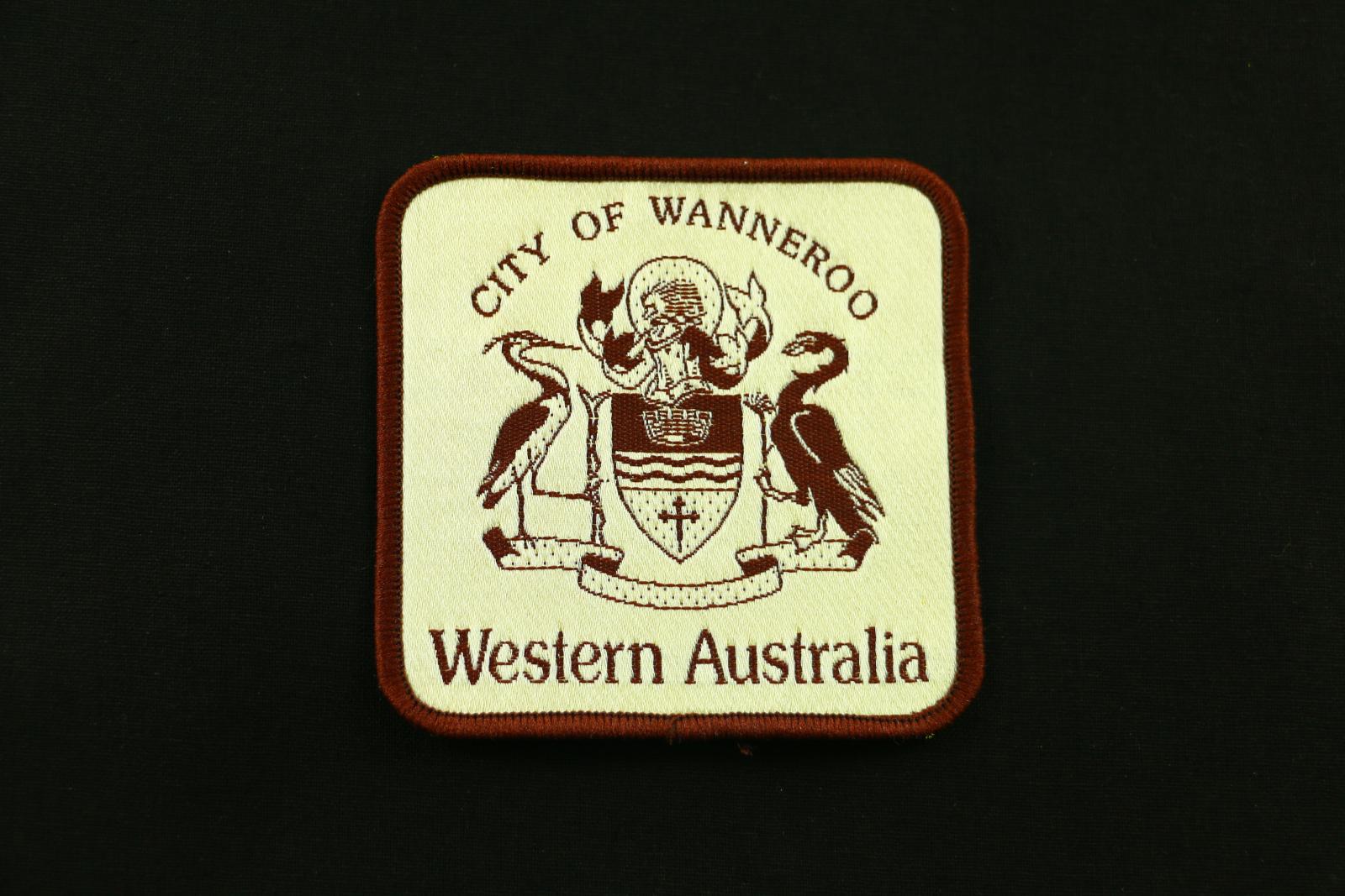 A square beige and brown City of Wanneroo cloth badge. The badge has 'CITY OF WANNEROO' written across the top and 'WESTERN AUSTRALIA' along the bottom in brown thread. The City of Wanneroo crest is in the middle of the writing in brown thread.