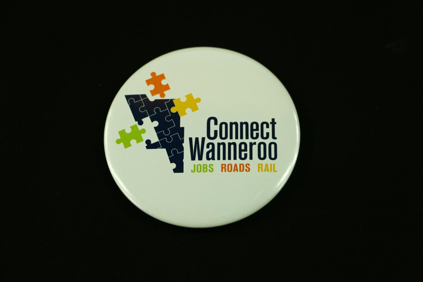 Circular Connect Waneroo badge. The front is white plastic with the 'Connect Wanneroo' logo and slogan. The back is silver metal with a pin mechanism.