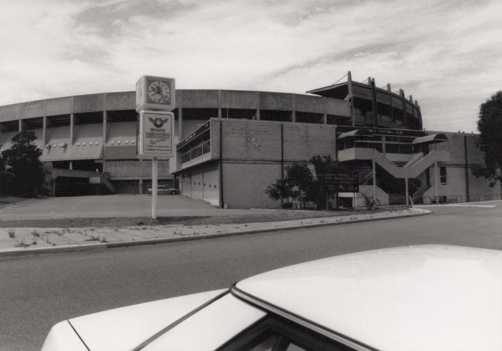 black and white photo of top of car, road, and large round building