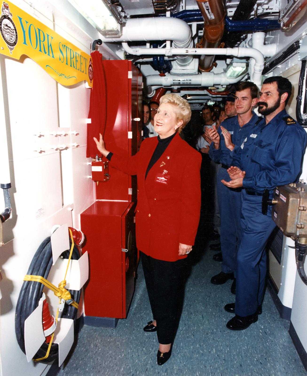 Colour photo of Albany mayor Annette Knight unveiling a York Street sign aboard HMAS ANZAC