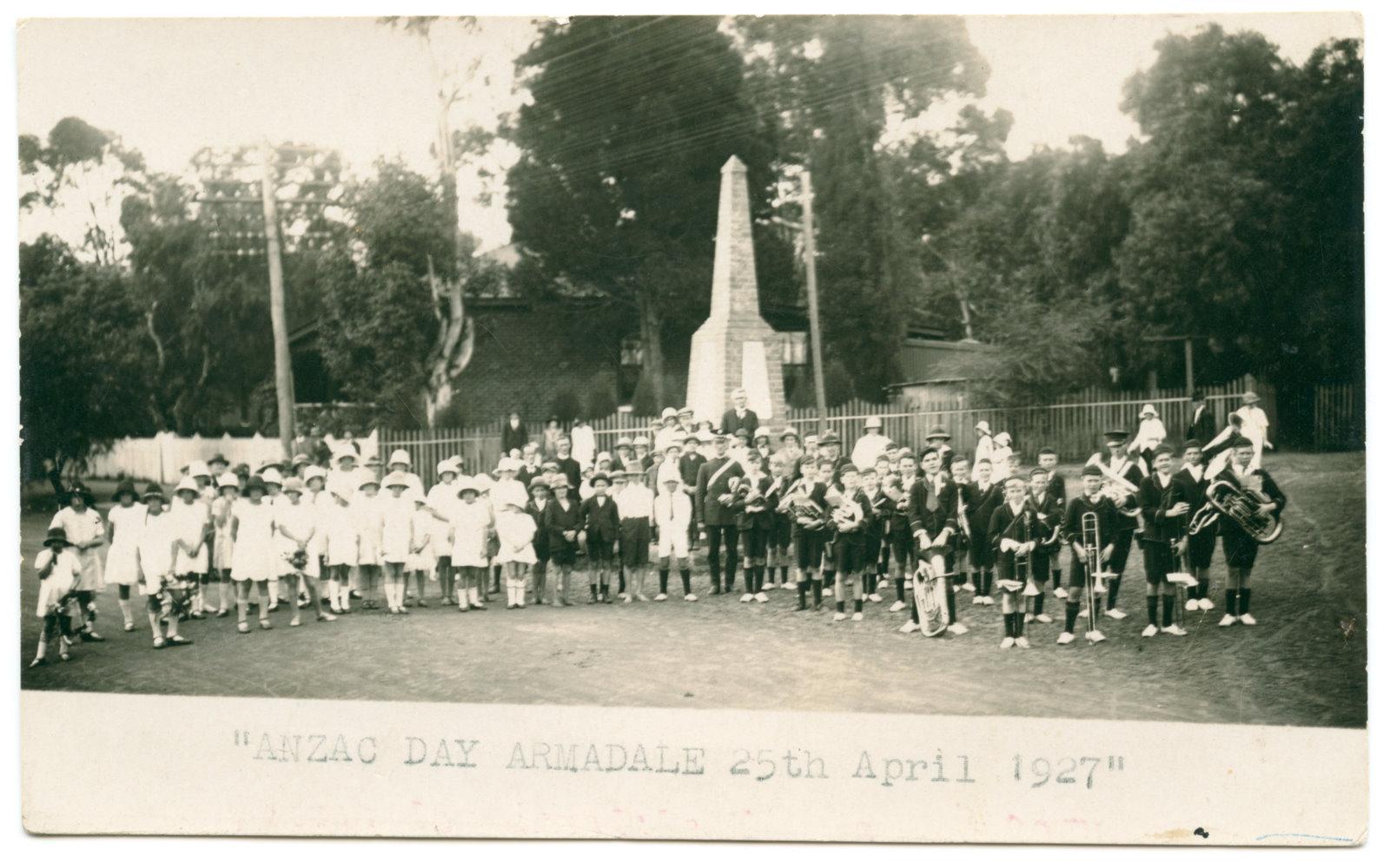 Black and white photograph of a group of children standing in front of a war memorial.