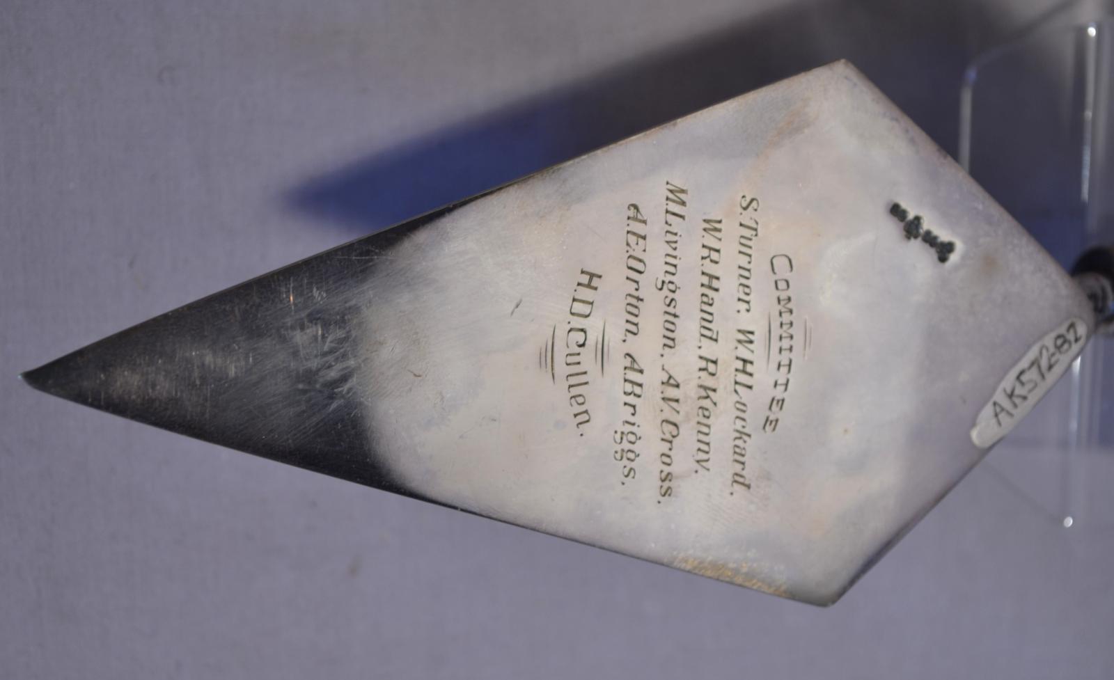 close up of engraved text on the back of a four sided diamond shaped silver trowel