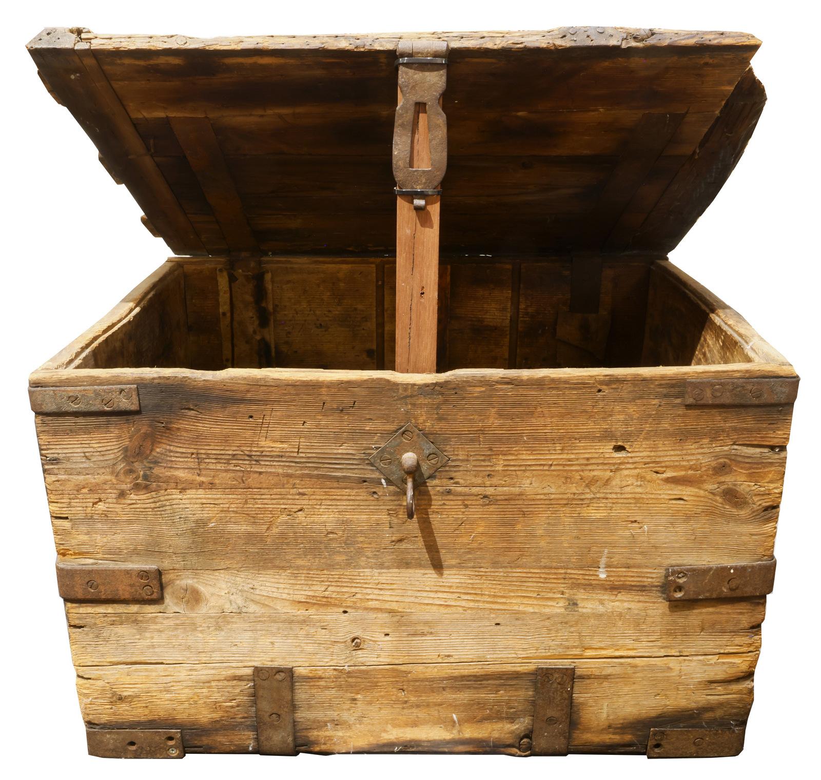 The image shows an old, rustic wooden chest with an open lid. The box appears to be constructed from rough-hewn planks, reinforced with metal bands and corner brackets. The wood shows signs of age, with weathered textures and patina, giving it a vintage or antique feel. A metal handle is visible on the front, and a wooden prop holds the lid open. The overall design suggests it could be used for storing heavy items, possibly something historical like cannonballs.