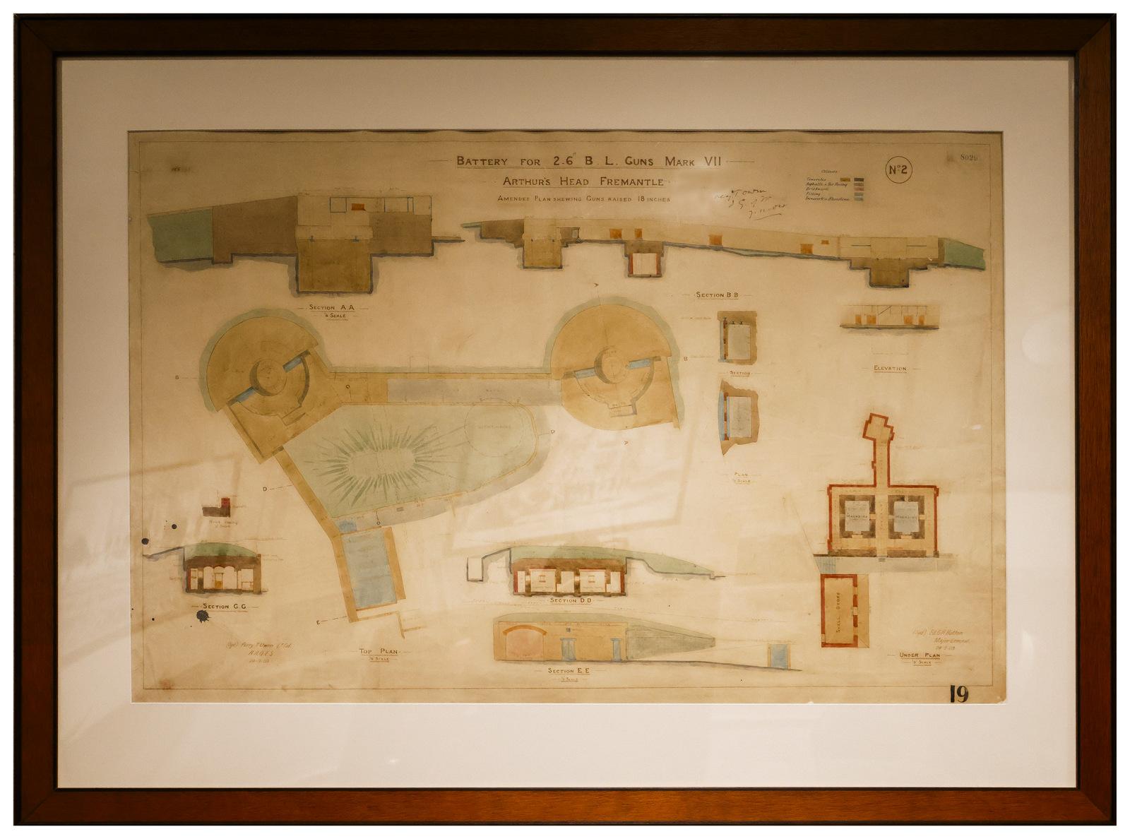 The image shows an architectural or engineering blueprint titled "Battery for 2.6' B.L. Guns Mark VII, Arthur's Head Fremantle." It depicts a detailed layout of a coastal defense battery with two circular gun emplacements and associated infrastructure at Arthur's Head, Fremantle. The plan is annotated with handwritten notes and features cross-sections of various structures, including a shelter, magazine, and other defensive facilities. The drawing includes elevation views of buildings and terrain, with colo