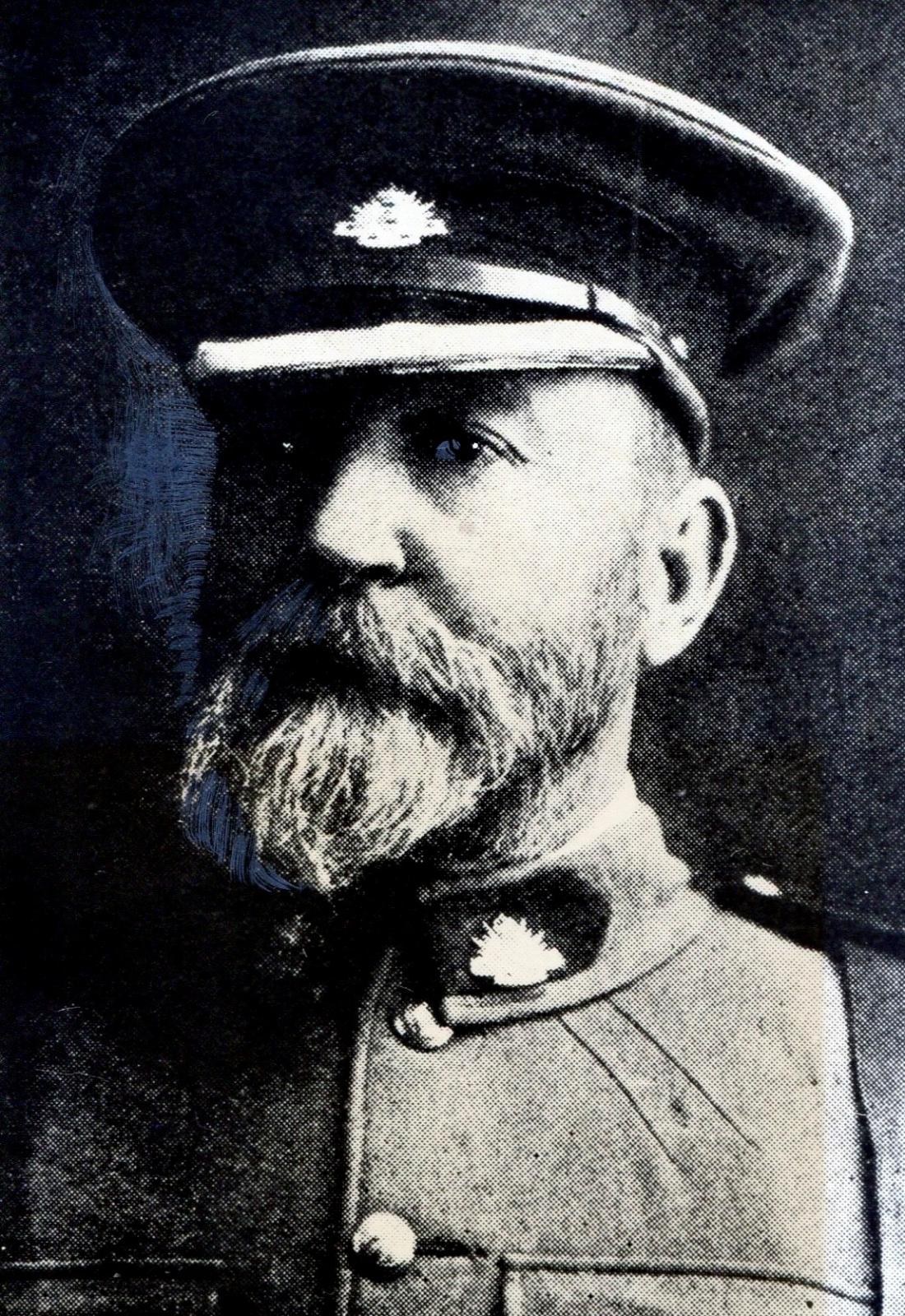 A historical black-and-white photograph of a man wearing a military uniform of the Goldfields Regiment, including a peaked cap adorned with an insignia. He has a thick beard and mustache, and his expression is serious, reflecting the formal portrait style of the era.