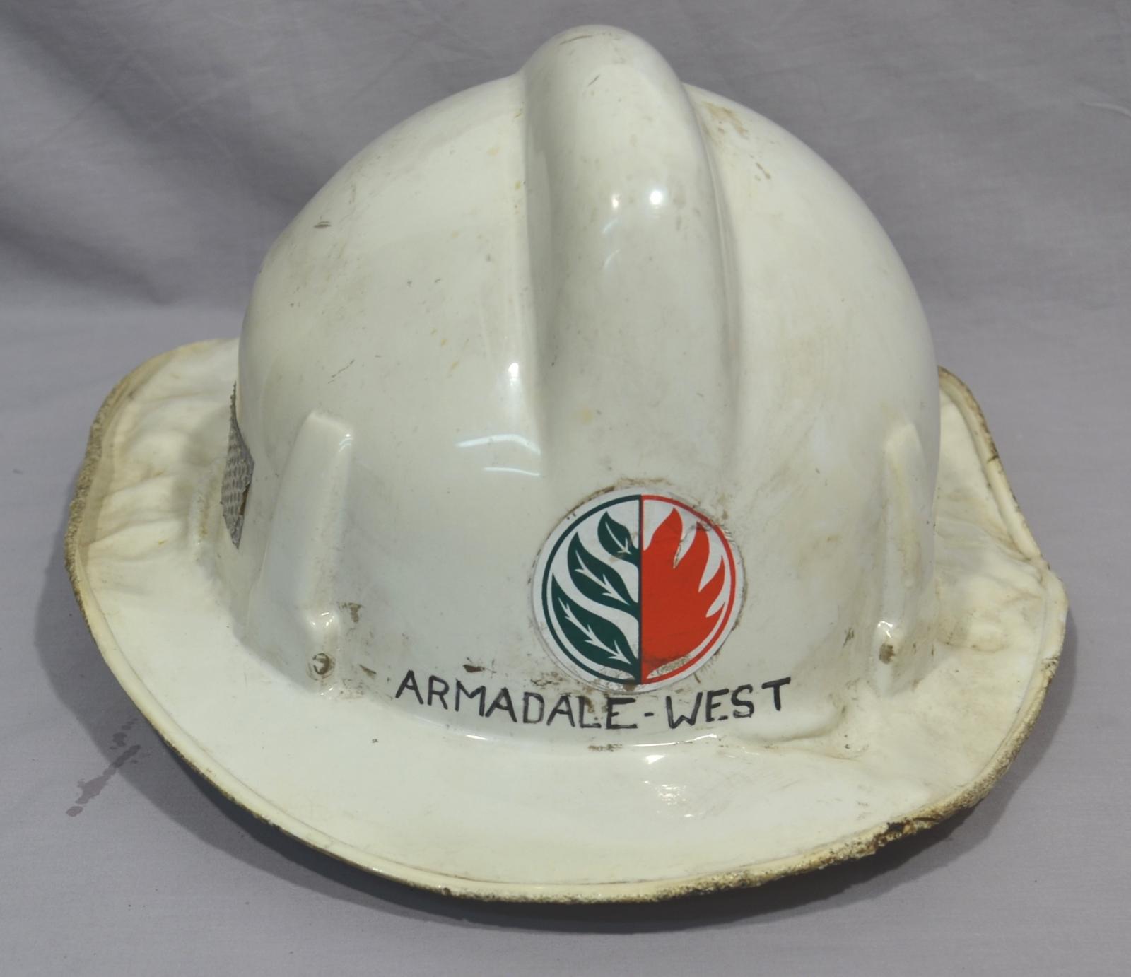 Cream coloured fireman's helmet with a ridge down the centre top. On the front is  circular sticker halved at the centre showing three leaves on the left and red flames on the right. The helmet has been damaged by heat on both sides.