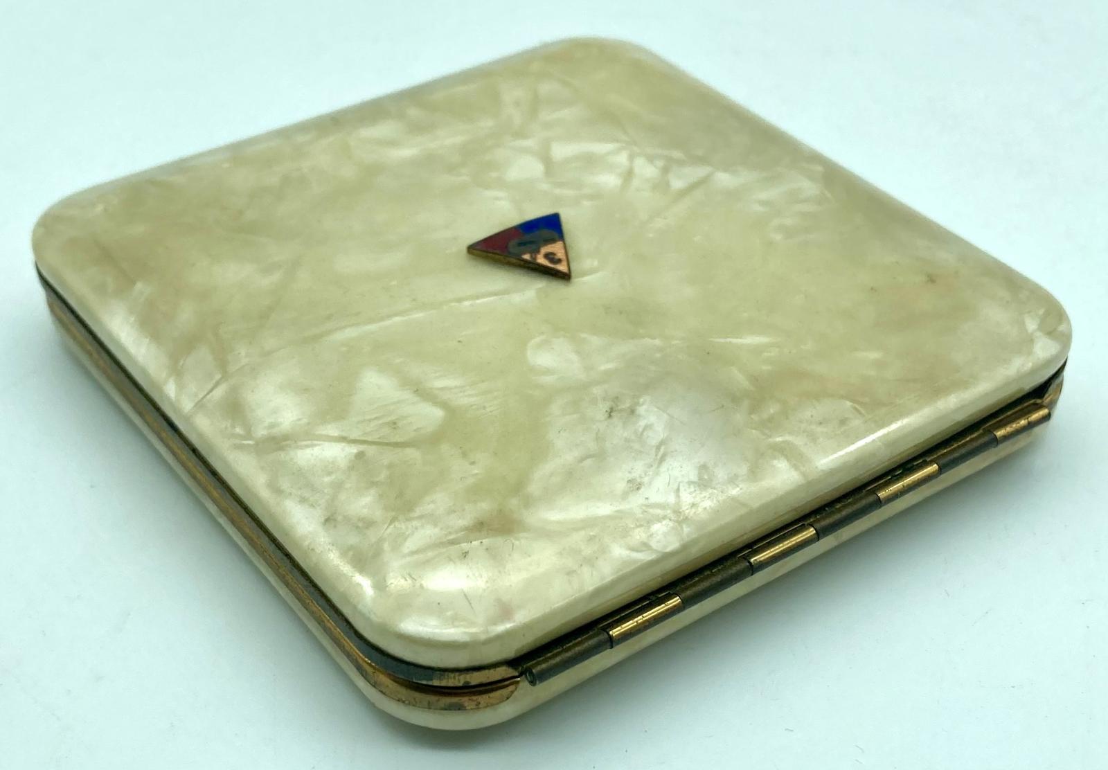 Oblique view of mother of pearl powder compact with enamel badge showing hinge