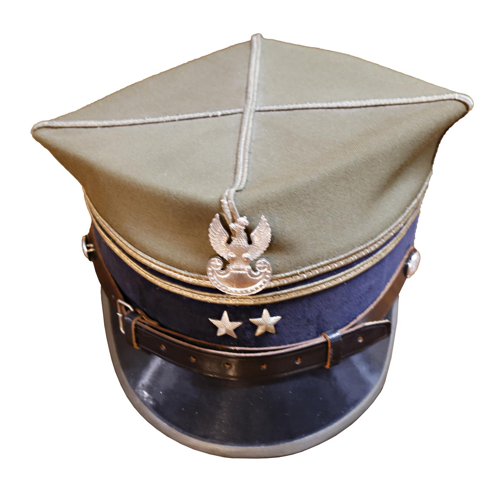 A Polish style military-style peaked cap featuring a khaki top, a navy blue band, and a silver emblem of an eagle with outstretched wings above two silver stars on the front. The cap has a leather strap across the front, fastened with buttons on either side